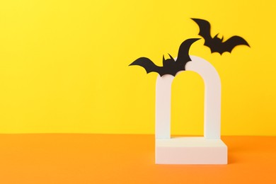 Photo of Halloween celebration. Podium and paper bats on orange table against yellow background, space for text