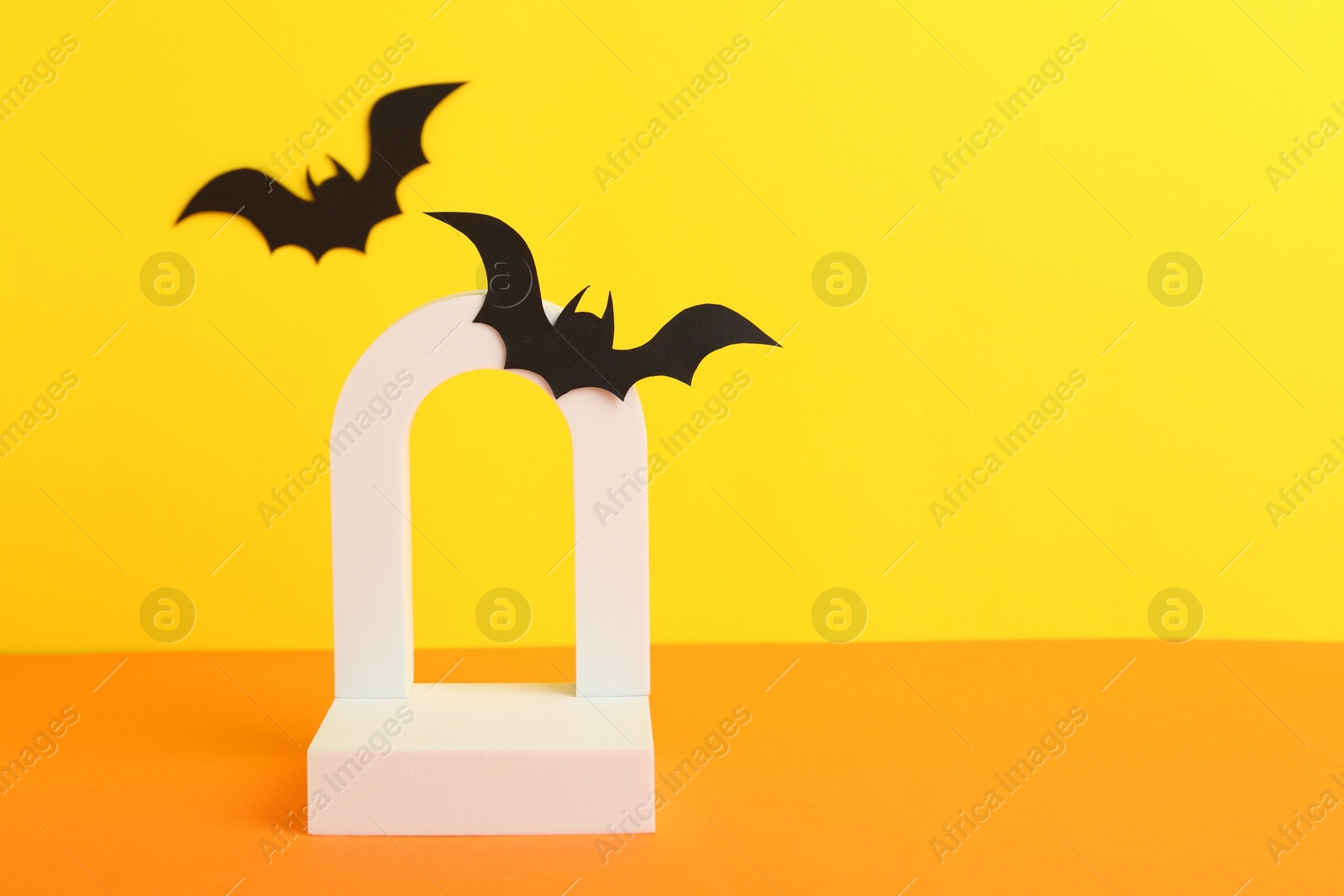 Photo of Halloween celebration. Podium and paper bats on orange table against yellow background, space for text