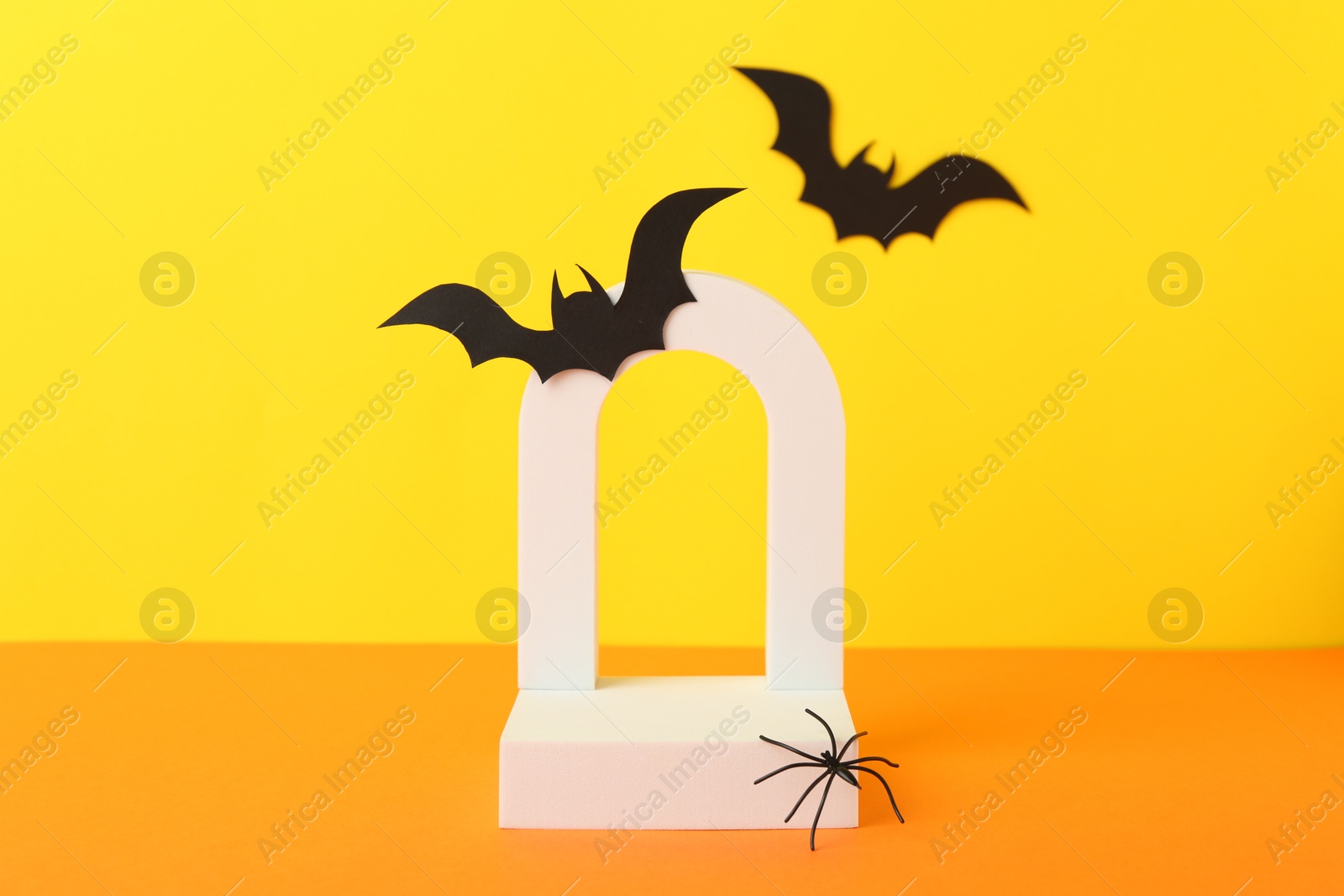 Photo of Presentation of product. Podium and Halloween decor on orange table against yellow background. Space for text