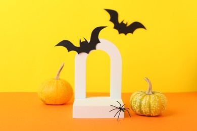 Photo of Presentation of product. Podium and Halloween decor on orange table against yellow background. Space for text