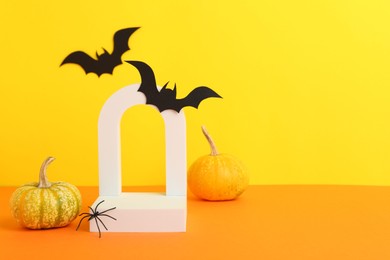 Photo of Presentation of product. Podium and Halloween decor on orange table against yellow background. Space for text