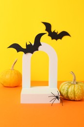 Photo of Presentation of product. Podium and Halloween decor on orange table against yellow background. Space for text