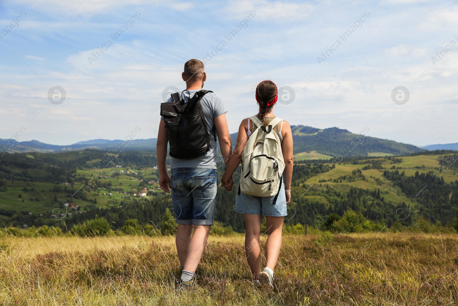 Photo of Couple with backpacks walking to mountains, back view. Active tourism