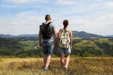 Photo of Couple with backpacks walking to mountains, back view. Active tourism