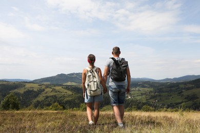 Photo of Couple with backpacks walking to mountains, back view. Active tourism