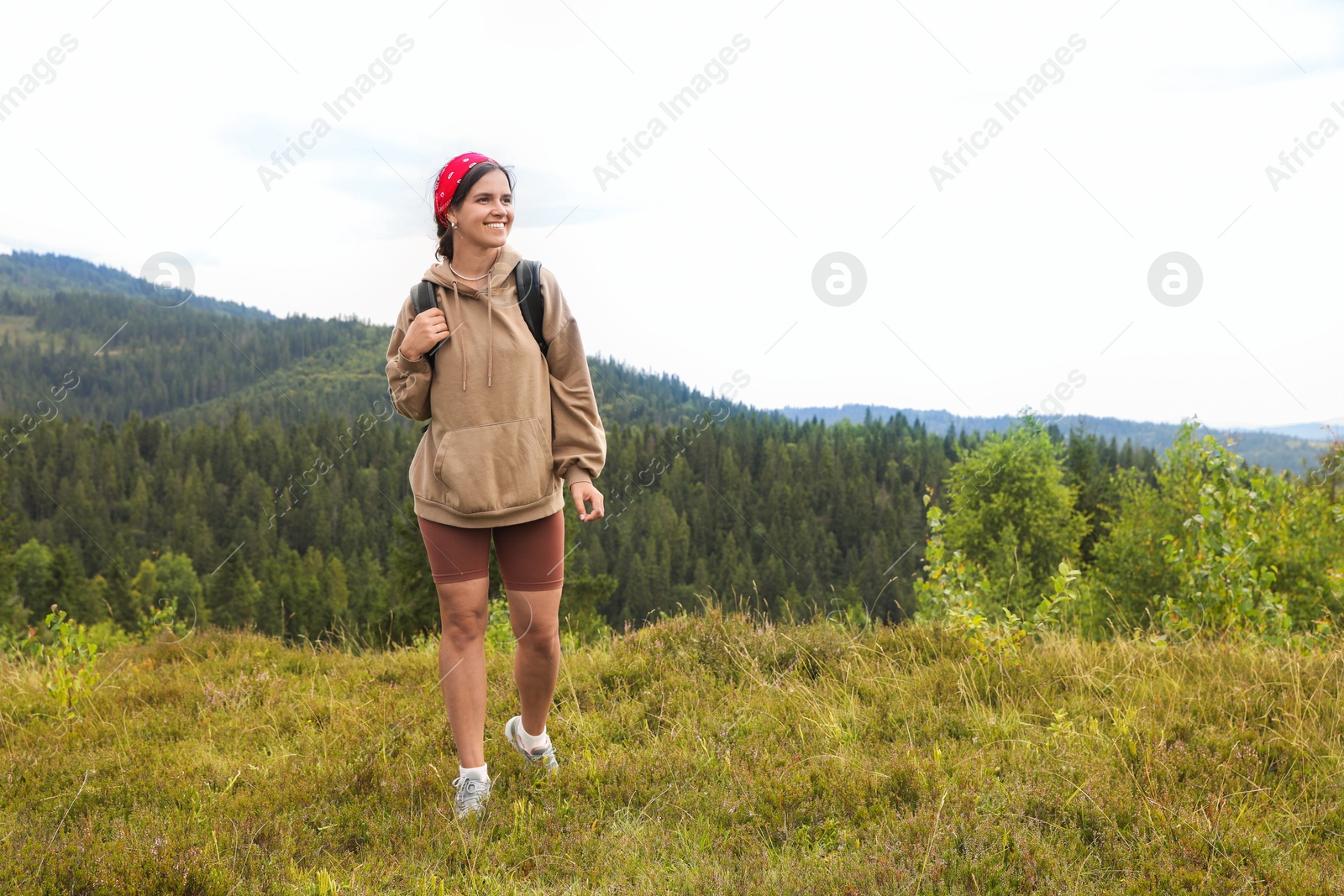 Photo of Smiling tourist with backpack walking in mountains. Space for text