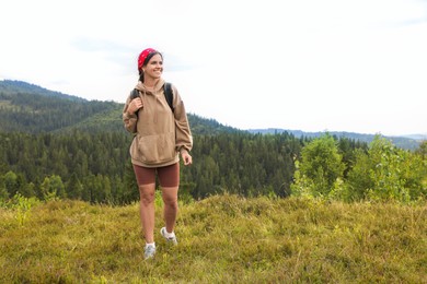 Smiling tourist with backpack walking in mountains. Space for text