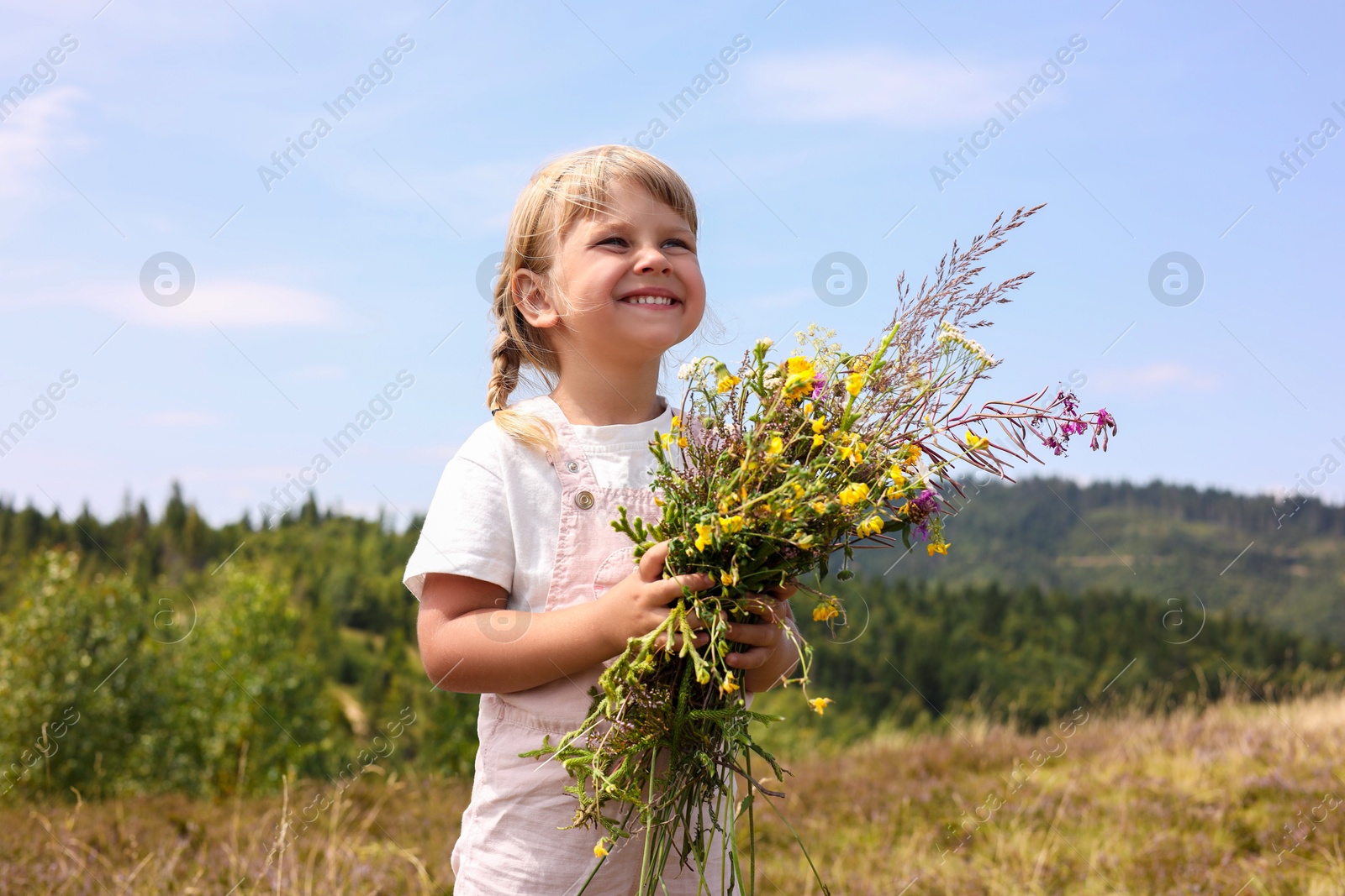 Photo of Smiling little girl with bouquet of wildflowers at field