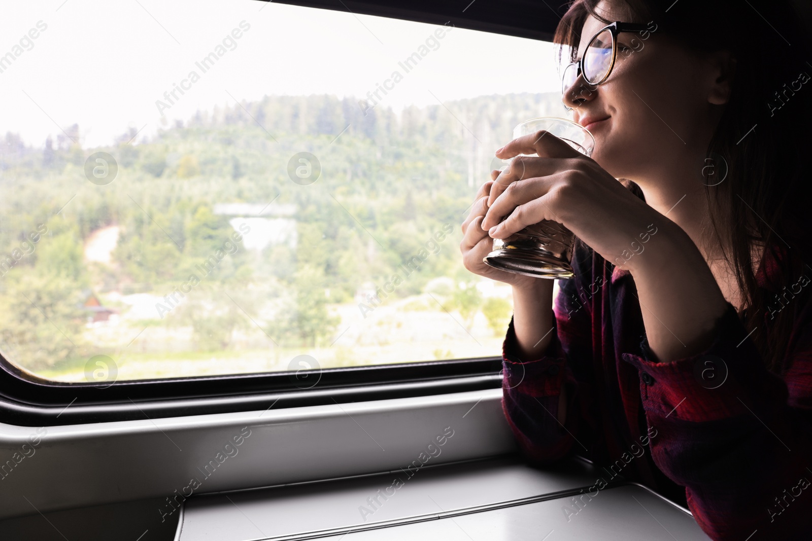 Photo of Young woman with cup of tea at table in train, space for text