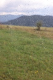 View of mountains through window with water droplets on rainy day, closeup