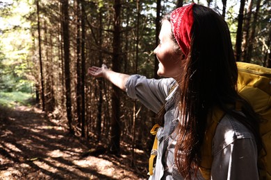 Young hiker with backpack showing something in forest