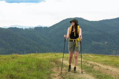 Young hiker with backpack and trekking poles in mountains, space for text