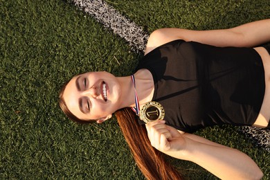 Photo of Happy winner with golden medal lying on green grass at stadium, top view