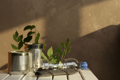 Photo of Recycling concept. Metal cans and plastic bottle with plants on white wooden table