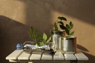 Photo of Recycling concept. Metal cans and plastic bottle with plants on white wooden table