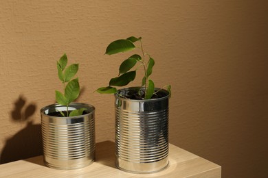 Photo of Recycling concept. Metal cans with plants on wooden table, space for text