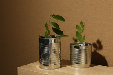 Photo of Recycling concept. Metal cans with plants on wooden table