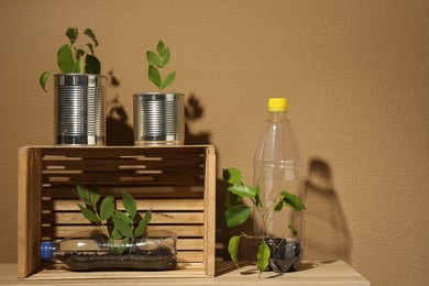 Photo of Recycling concept. Metal cans, plastic bottles and crate with plants on wooden table