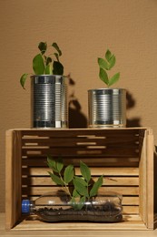 Photo of Recycling concept. Metal cans, plastic bottles and crate with plants on wooden table