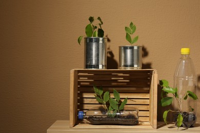 Photo of Recycling concept. Metal cans, plastic bottles and crate with plants on wooden table, space for text