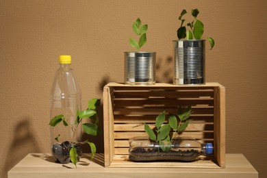 Photo of Recycling concept. Metal cans, plastic bottles and crate with plants on wooden table