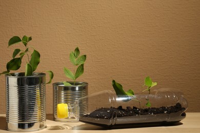 Photo of Recycling concept. Metal cans and plastic bottle with plants on wooden table, space for text