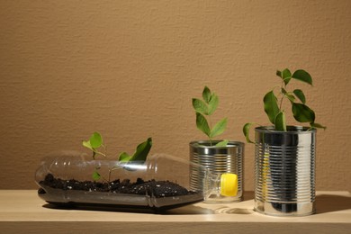 Photo of Recycling concept. Metal cans and plastic bottle with plants on wooden table, space for text