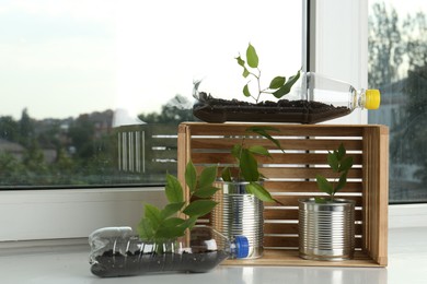 Photo of Recycling concept. Metal cans, plastic bottles and wooden crate with plants on windowsill