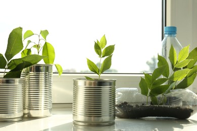 Photo of Recycling concept. Metal cans and plastic bottles with plants on windowsill