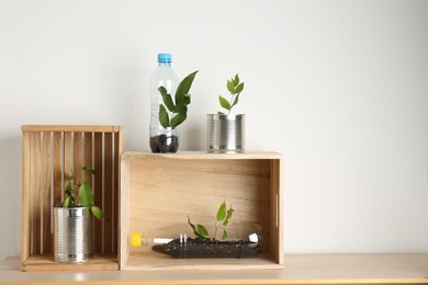 Photo of Recycling concept. Metal cans and plastic bottles with plants on wooden table, space for text