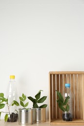 Photo of Recycling concept. Metal cans and plastic bottles with plants on wooden table, space for text