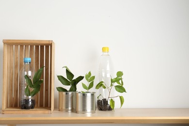 Photo of Recycling concept. Metal cans and plastic bottles with plants on wooden table, space for text