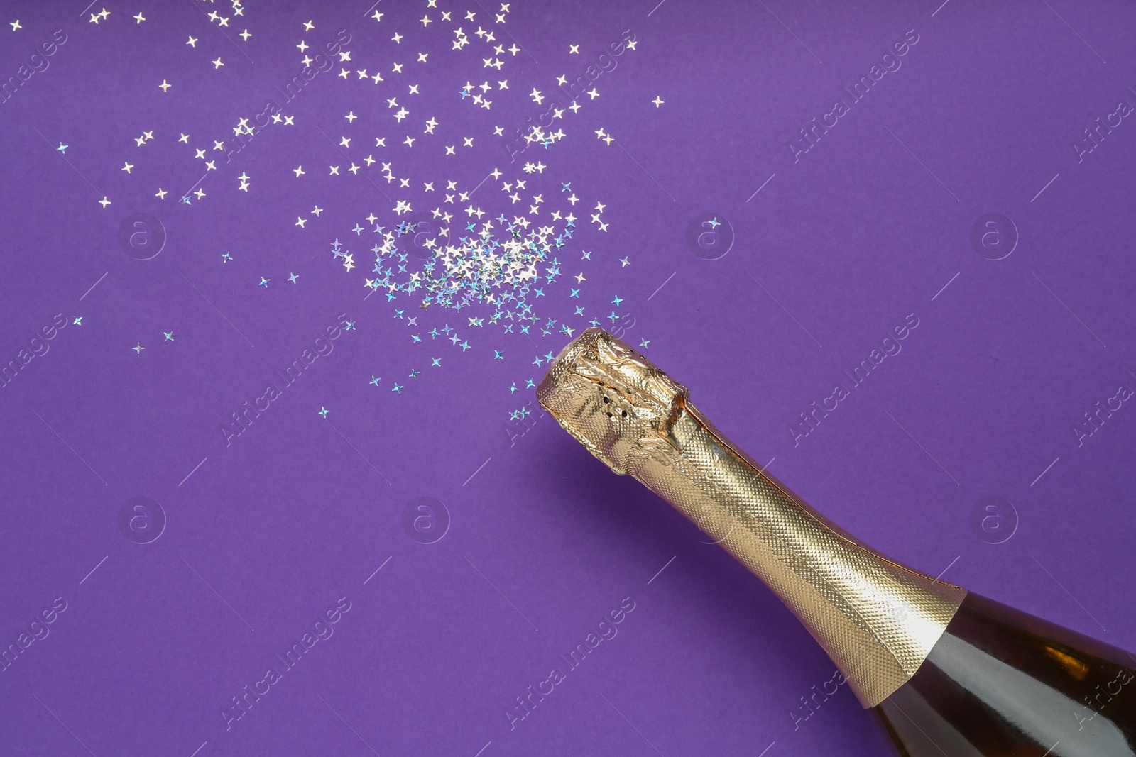 Photo of Bottle of sparkling wine and confetti on purple background, top view