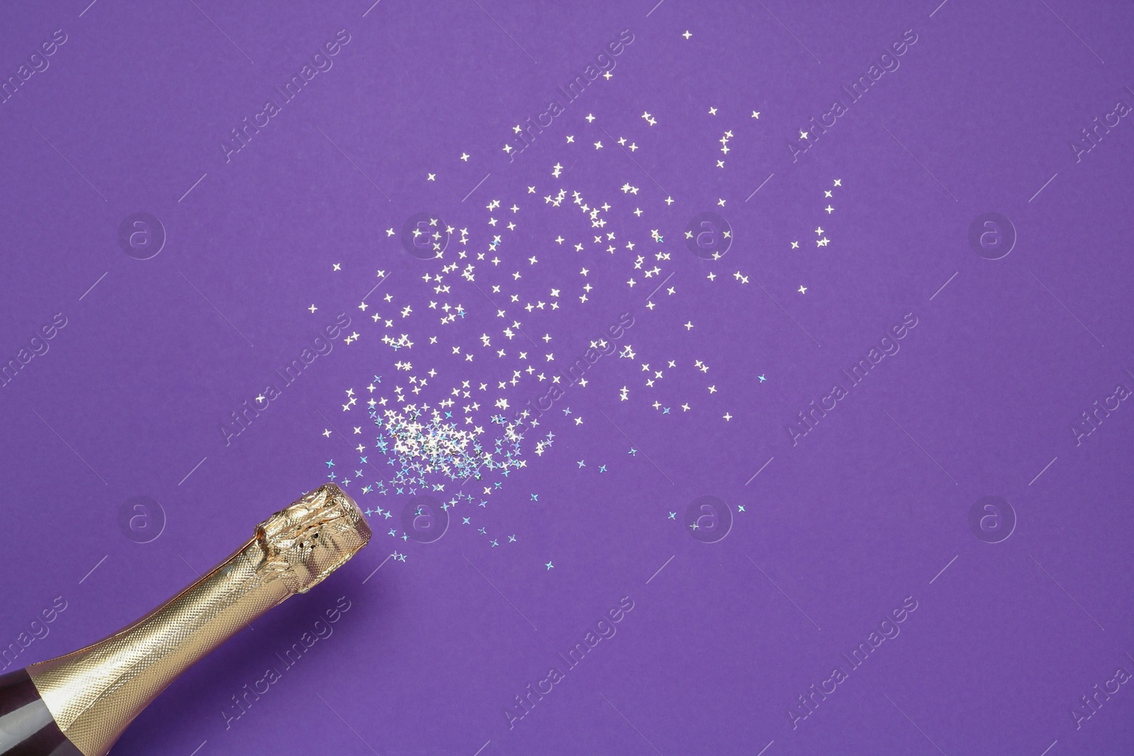 Photo of Bottle of sparkling wine and confetti on purple background, top view