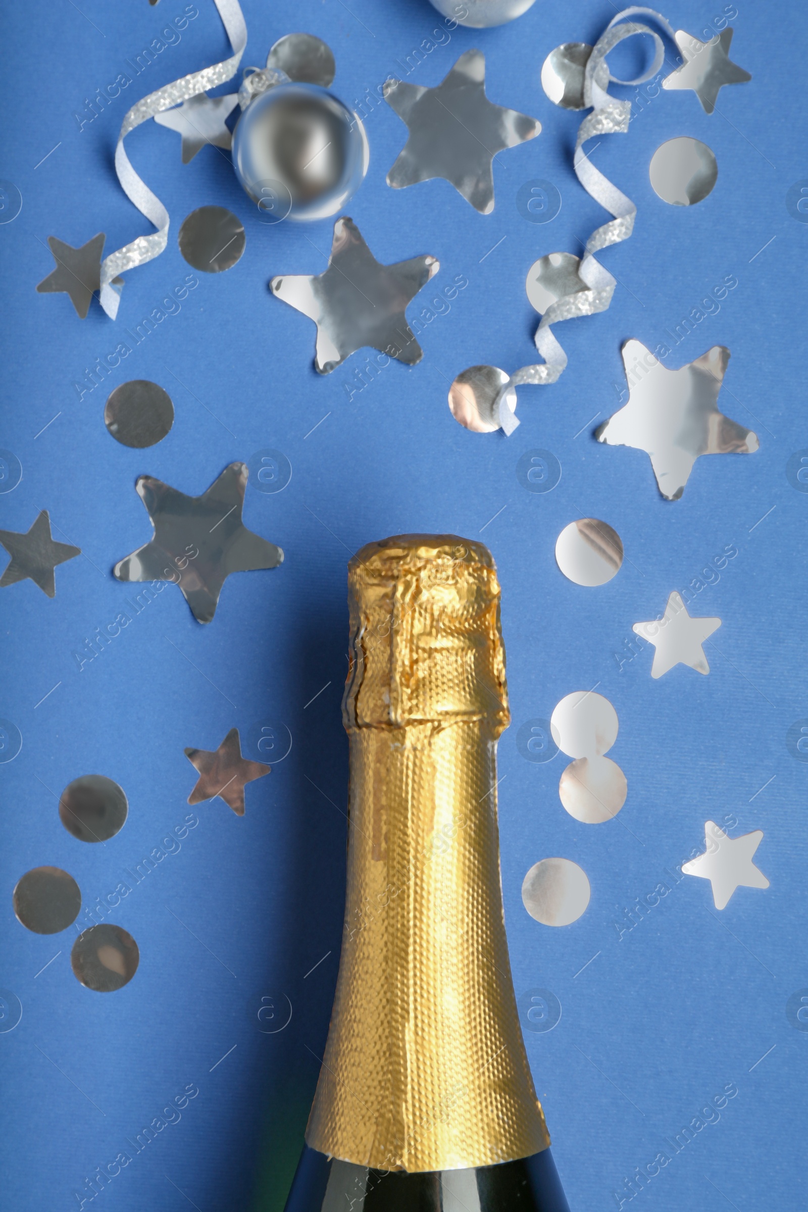 Photo of Bottle of sparkling wine and confetti on blue background, top view