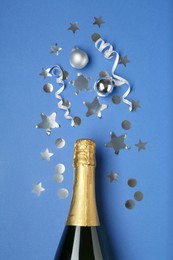 Photo of Bottle of sparkling wine and confetti on blue background, top view