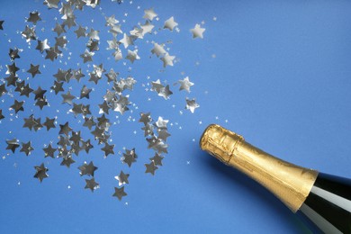 Photo of Bottle of sparkling wine and confetti on blue background, top view