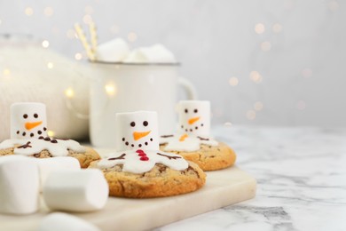 Photo of Delicious cookies with snowmen made of marshmallows on white table, closeup