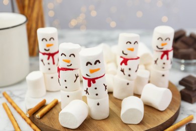 Photo of Funny snowmen made with marshmallows on white marble table, closeup