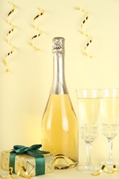 Photo of Shiny confetti, streamers, sparkling wine and gift box on beige background