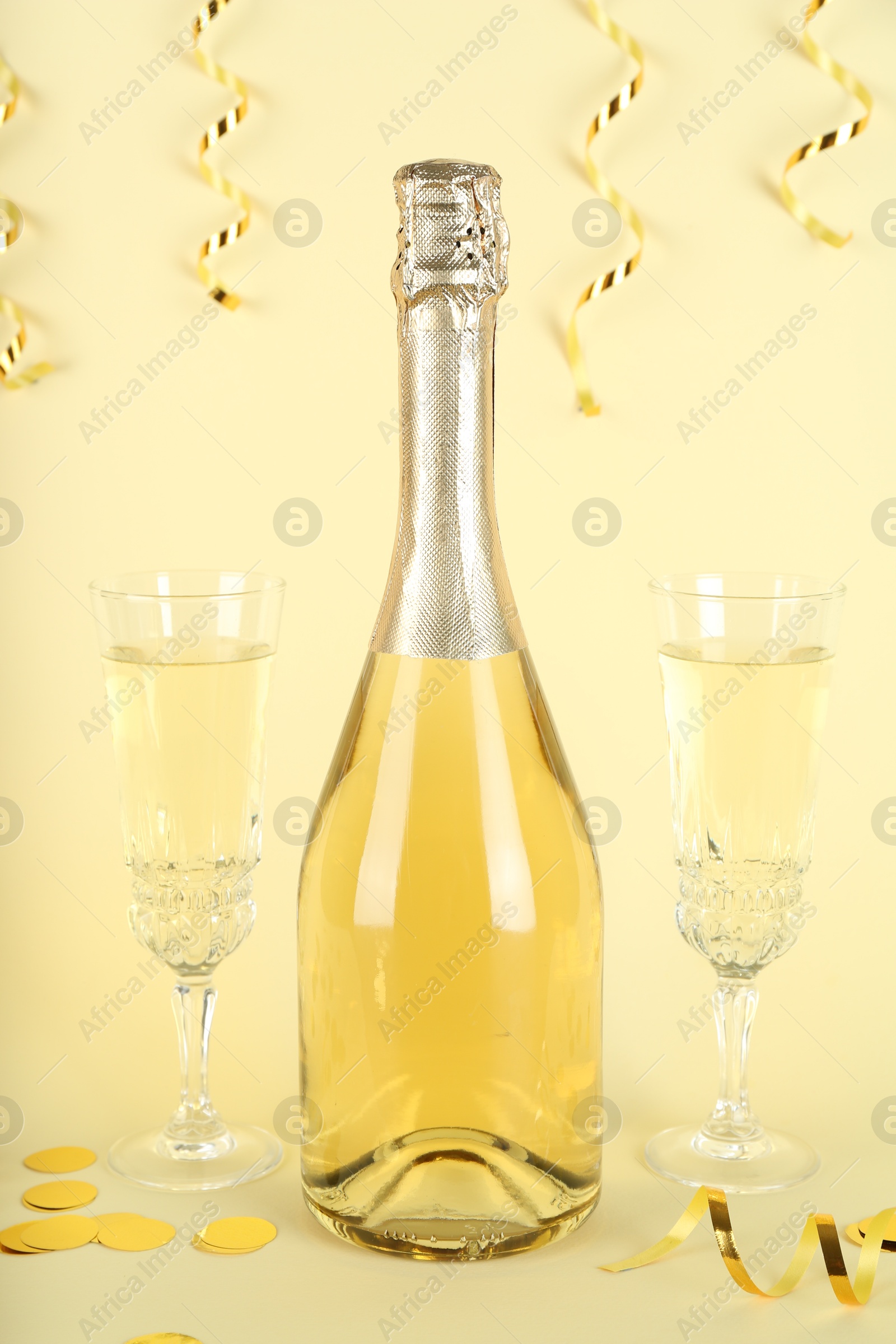 Photo of Shiny confetti, streamers and sparkling wine on beige background