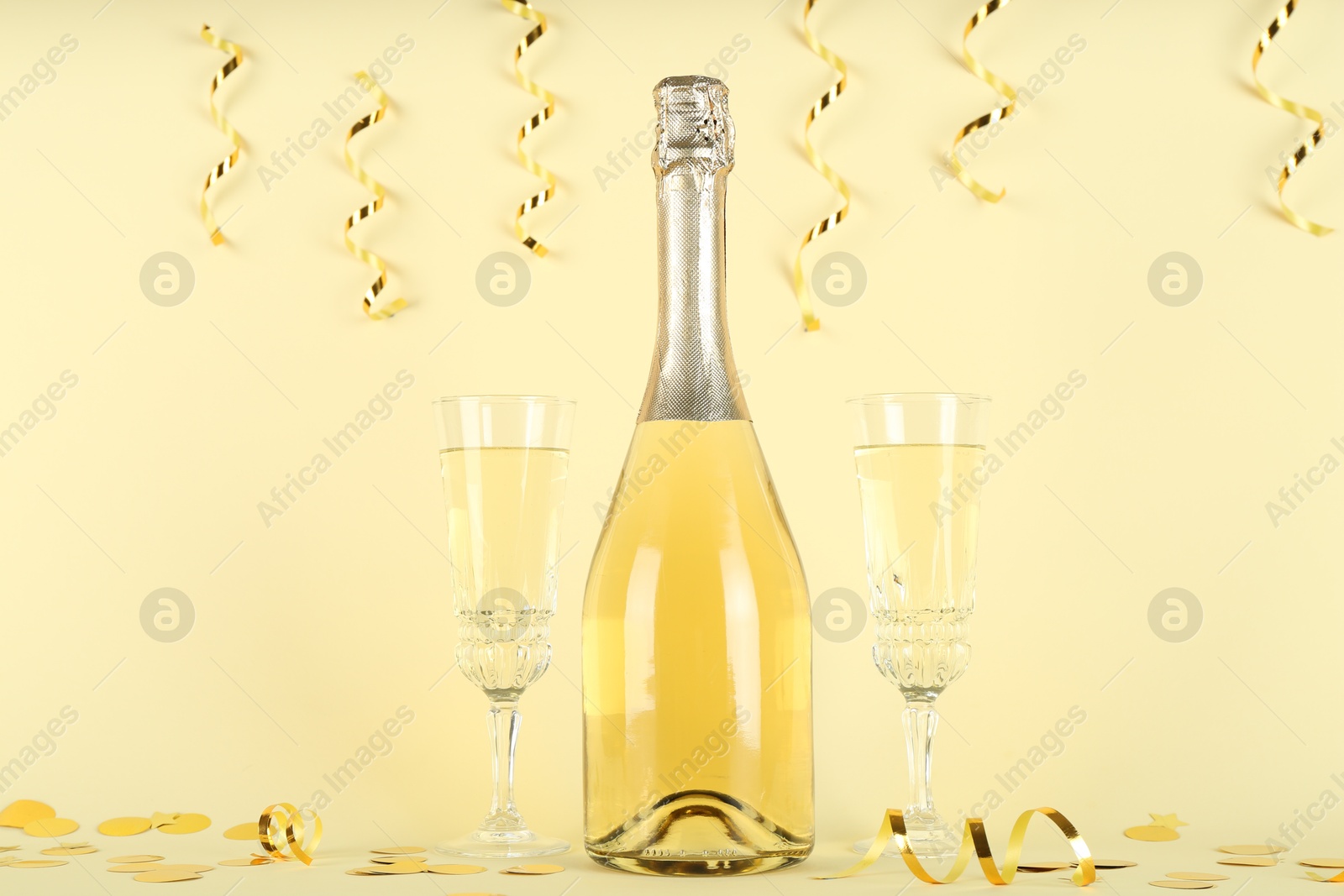 Photo of Shiny confetti, streamers and sparkling wine on beige background