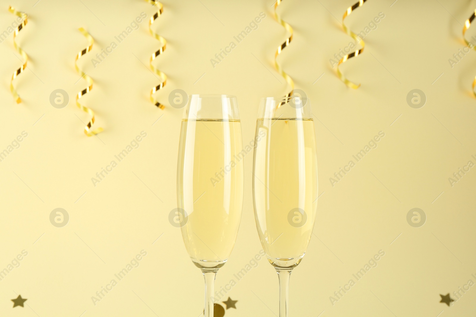 Photo of Glasses of sparkling wine, shiny confetti and streamers on beige background