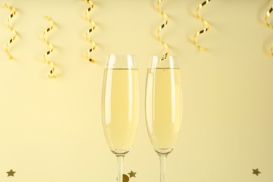 Photo of Glasses of sparkling wine, shiny confetti and streamers on beige background