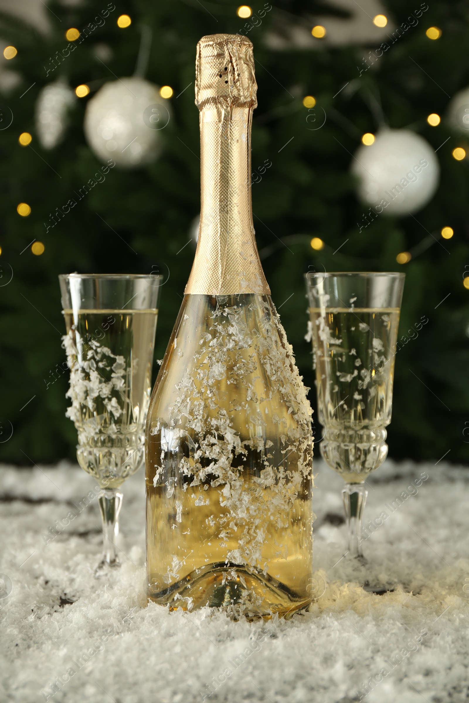 Photo of Sparkling wine in bottle, glasses and artificial snow against blurred lights