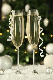 Photo of Sparkling wine in glasses, baubles and artificial snow on blurred background