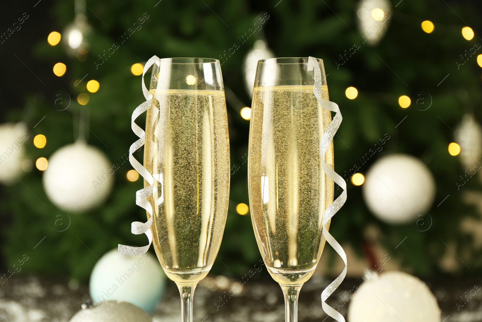 Photo of Sparkling wine in glasses and streamers on blurred background, closeup