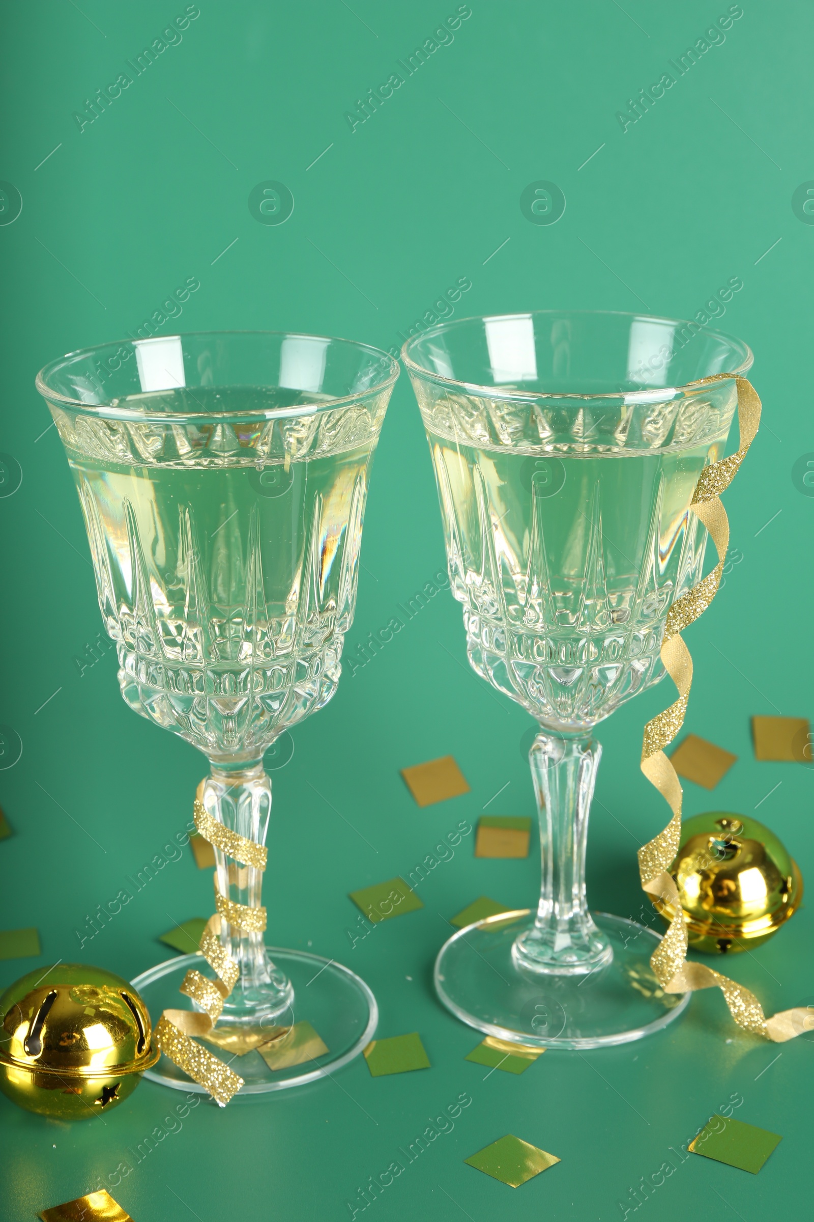 Photo of Sparkling wine in glasses, confetti and other Christmas decor on green background