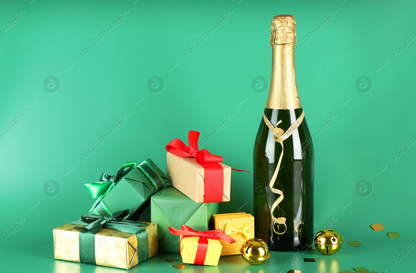 Photo of Bottle with sparkling wine, confetti and gift boxes on green background