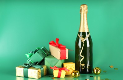 Photo of Bottle with sparkling wine, confetti and gift boxes on green background